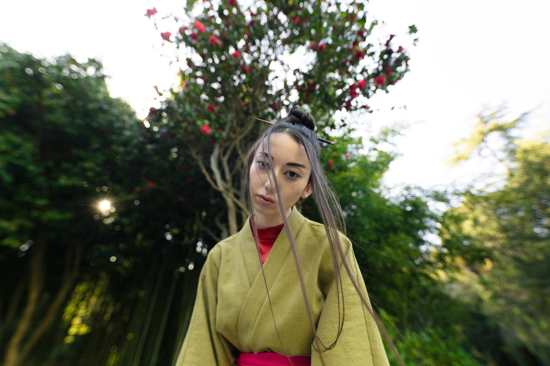 woman in green kimono standing near tall trees
